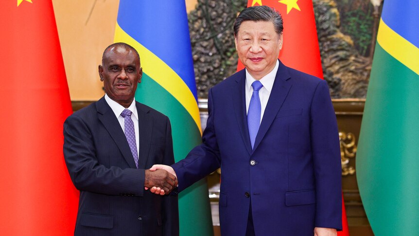 Jeramiah Manele shakes hands with Xi Jinping standing in front of the flags of Solomon Islands and China
