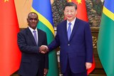 Jeramiah Manele shakes hands with Xi Jinping standing in front of the flags of Solomon Islands and China