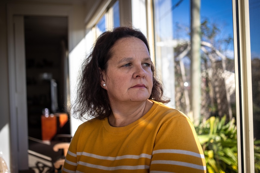 A woman sits next to a window, look to the side of the camera.