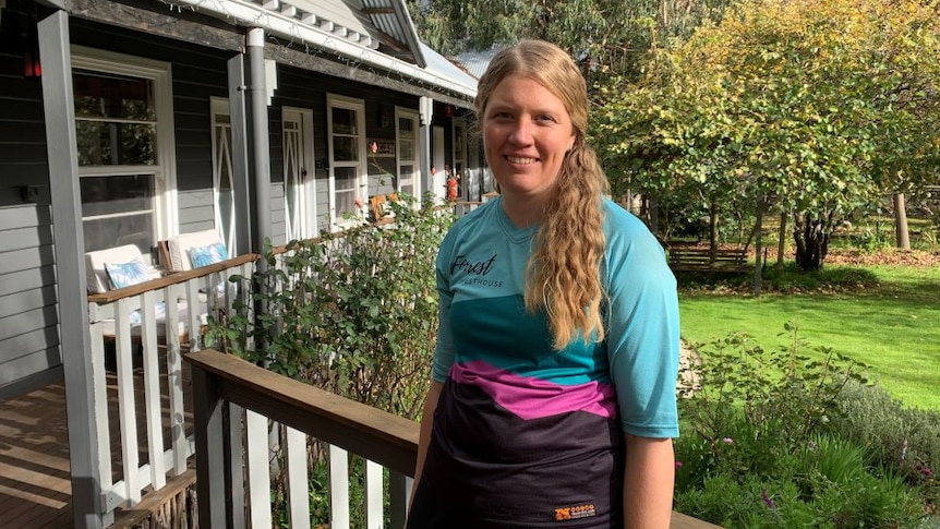 A woman with long blonde hair stands on the verandah of a country guesthouse.