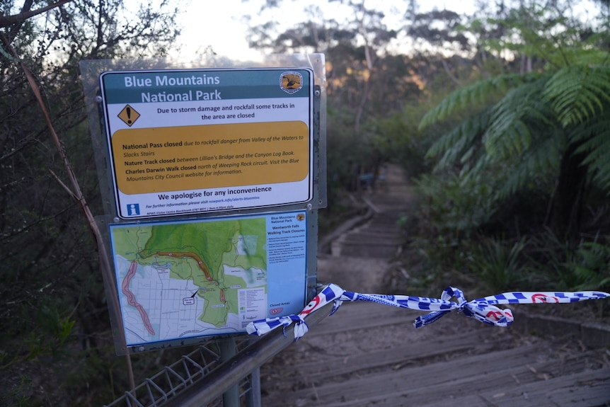 A sign with bushwalking information with police tape blocking a walkway