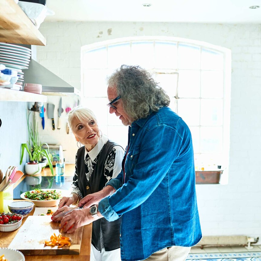 A grey-haired man in kitchen cooking for a grey-haired woman