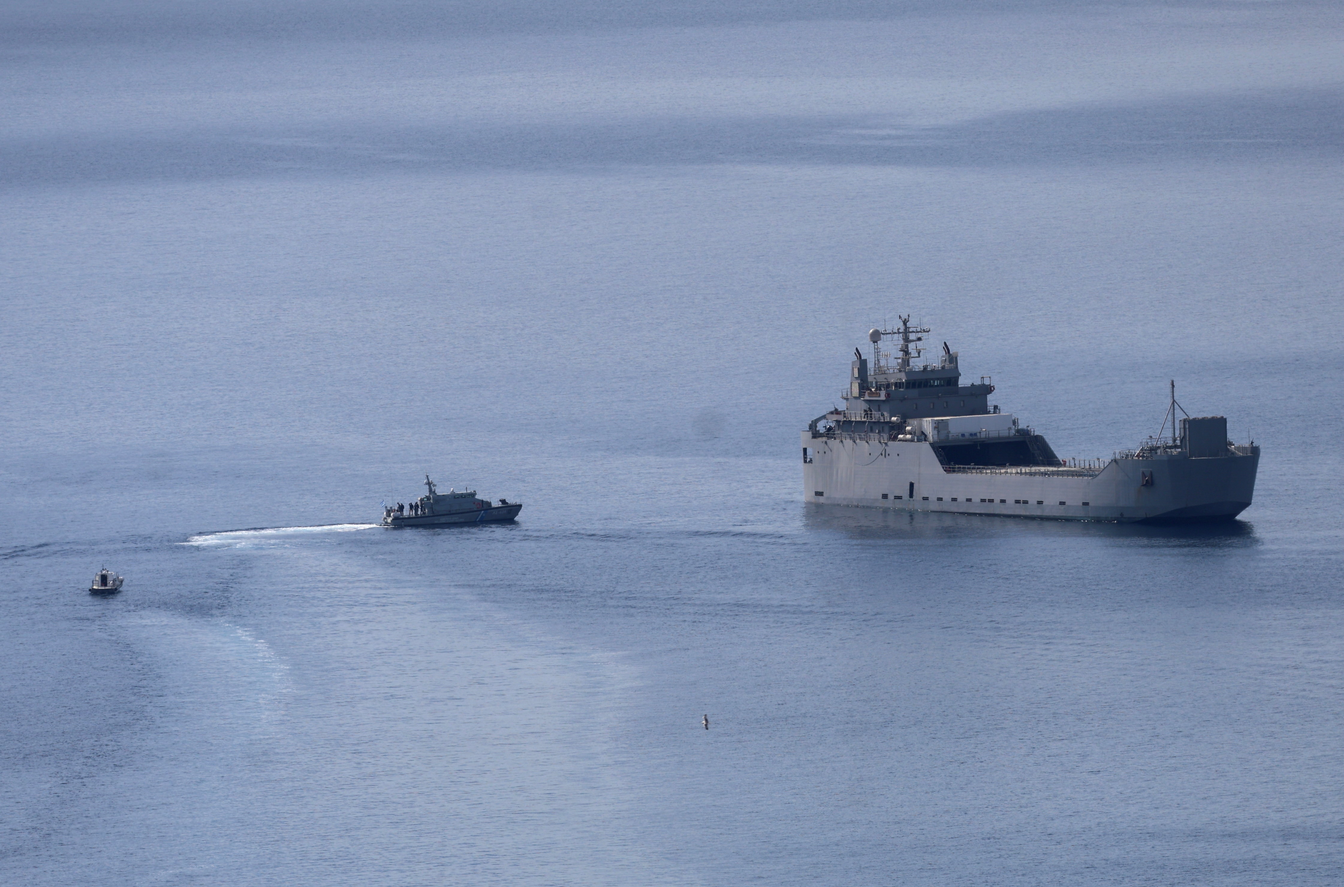 A small boat approaches a large vessel in the ocean.