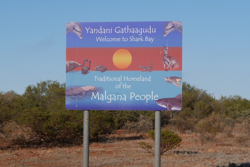 A close shot of a sign with a welcome to Shark Bay in English and Malgana