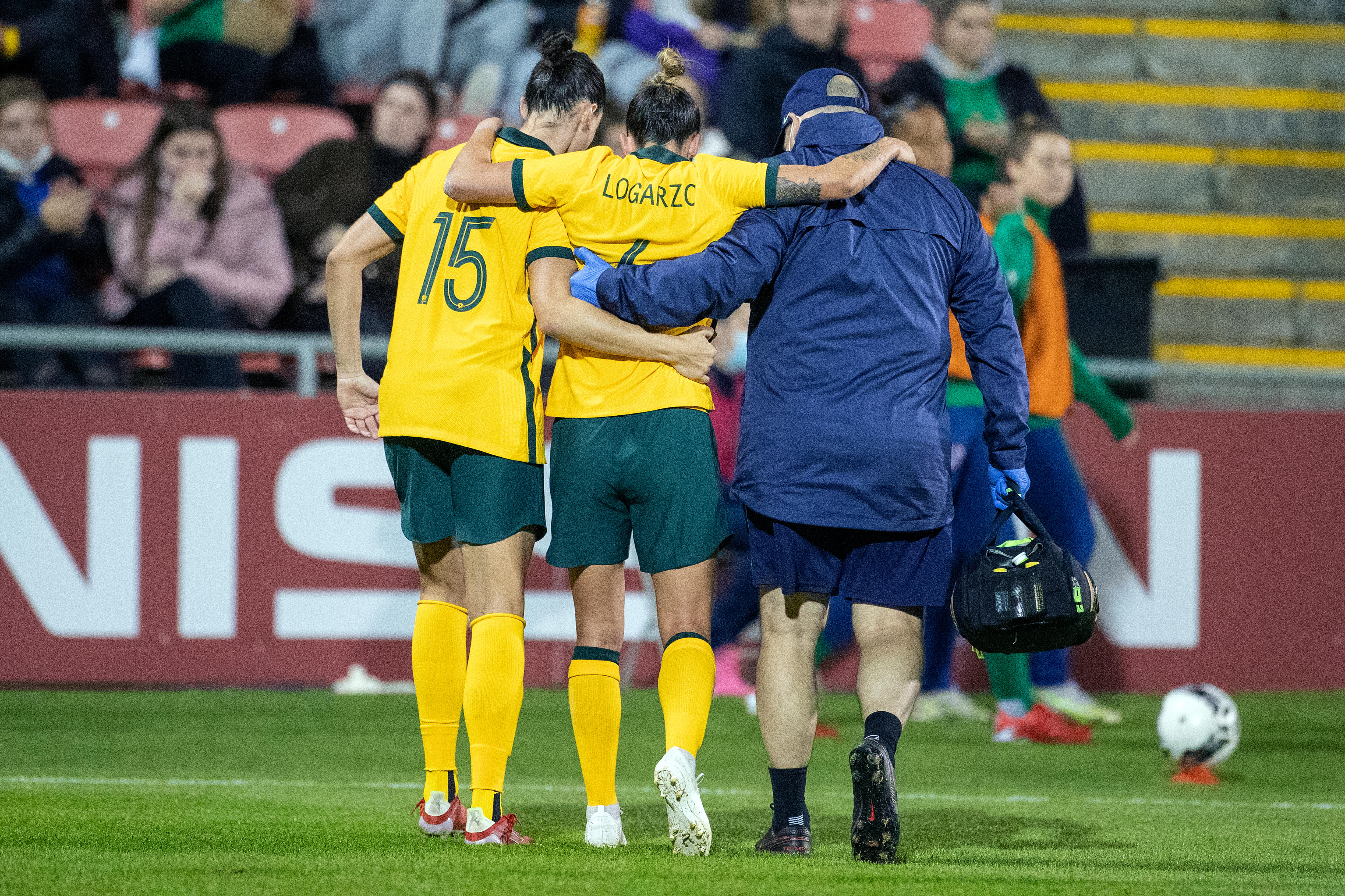 Matildas player Chloe Logarzo is helped off the field by a teammate and trainer after an injury in a game against Ireland.