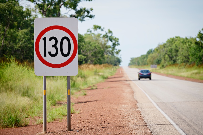 A car drives past 130km/h speed signage on the Stuart Highway, on a sunny day.