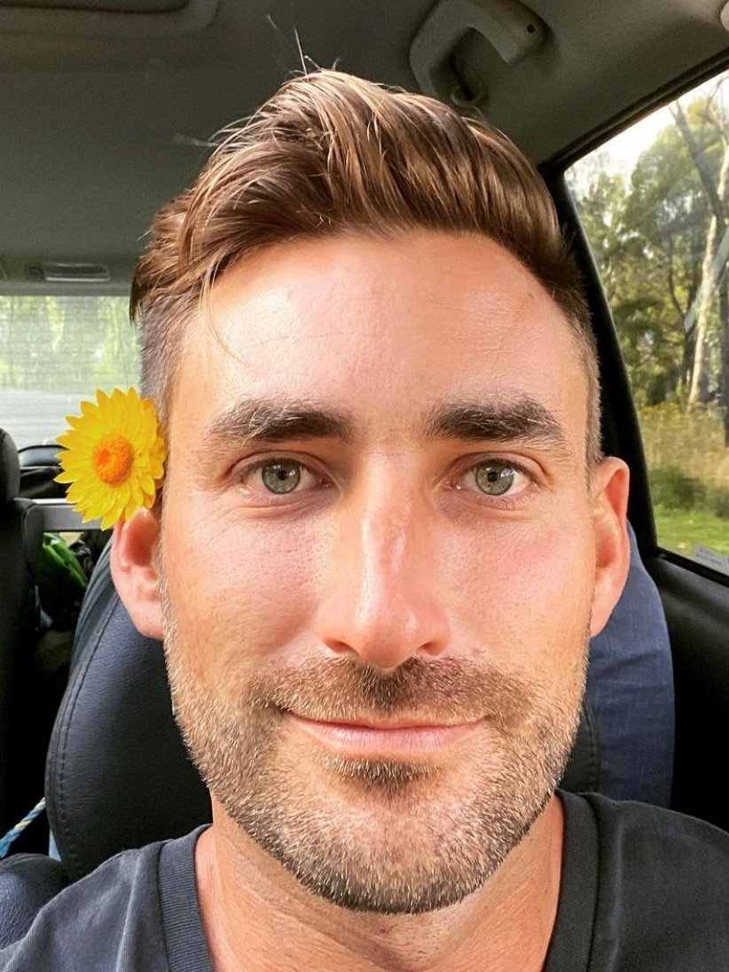 a selfish of a man with a yellow daisy behind his ear