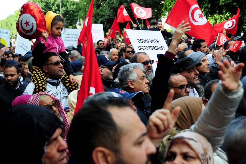 Tunisians gather holding Tunisian flags during a protest.