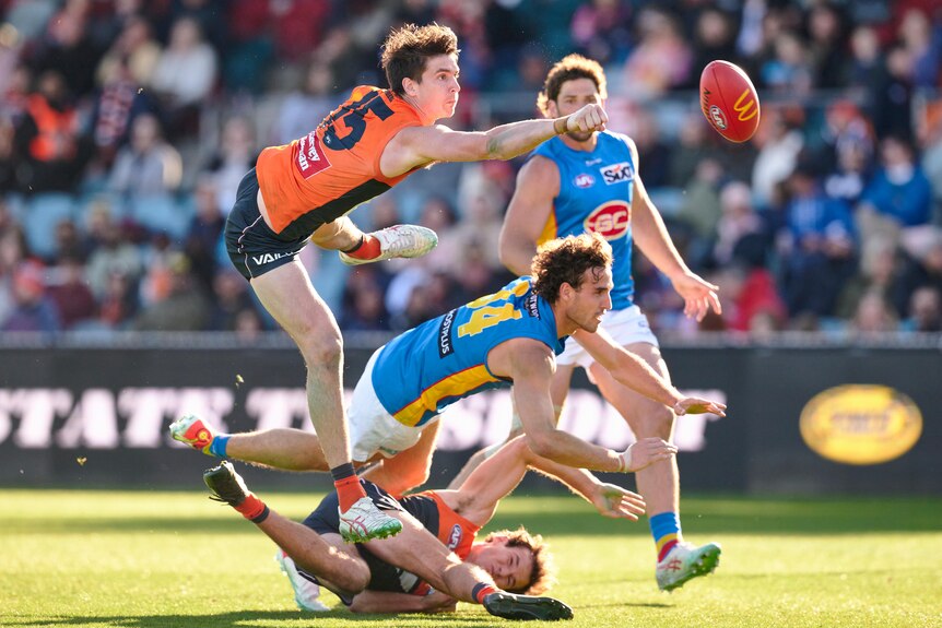A Giants' AFL player uses his fist to punch the ball clear of a Suns forward during a game.