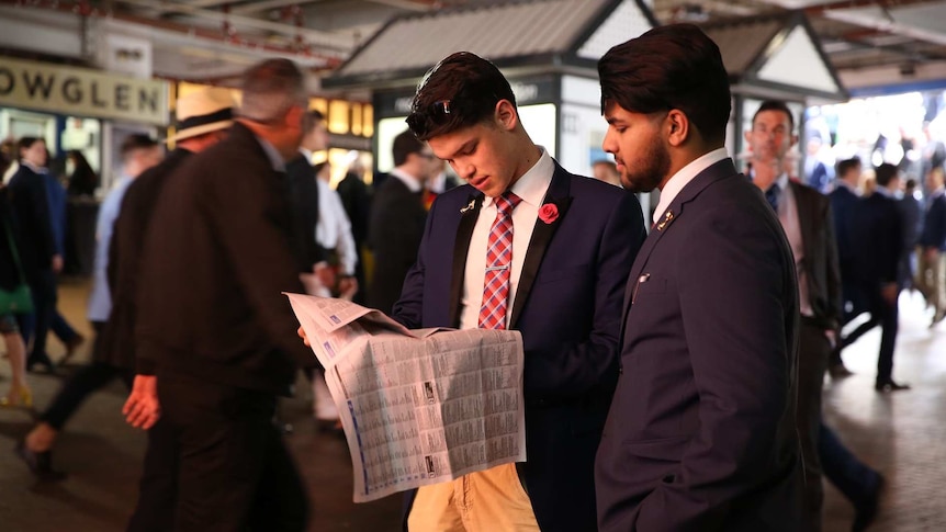 Two men wearing suits checking the form guide at the Melbourne Cup.