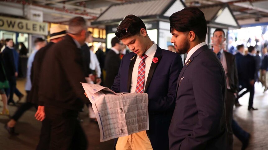 Two men wearing suits checking the form guide at the Melbourne Cup.