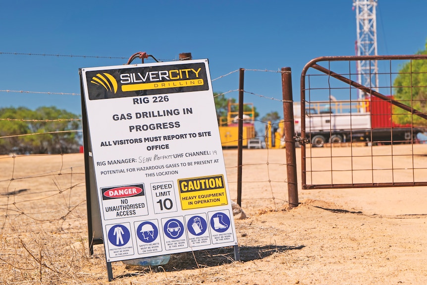 A sign details oil and gas drilling in place, with a gate behind it