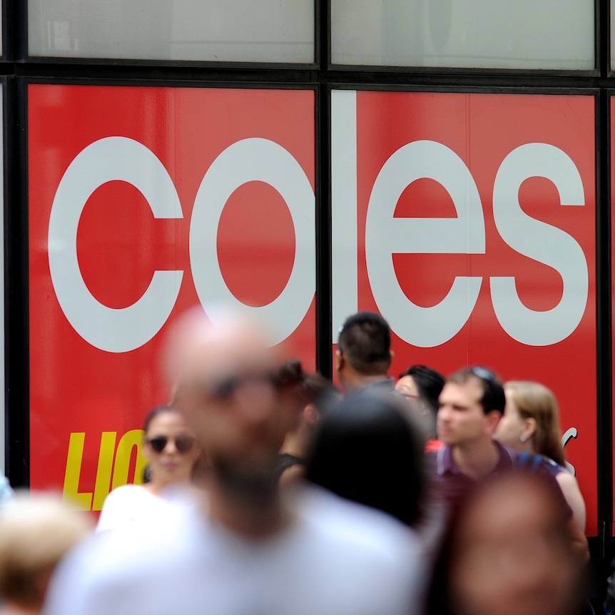 A crowd of out-of-focus people walk in front of a large in-focus Coles supermarket sign.