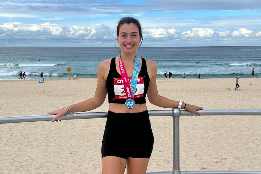 Lili stands near a beach wearing a City to Surf medal and running shorts and top.