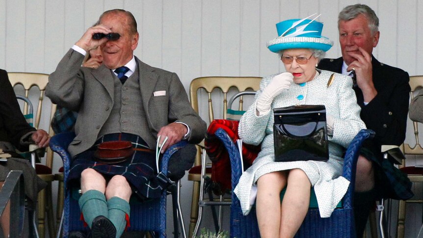 Queen Elizabeth II applies lipstick as she sits next to her husband Prince Phillip, who is looking through binoculars.