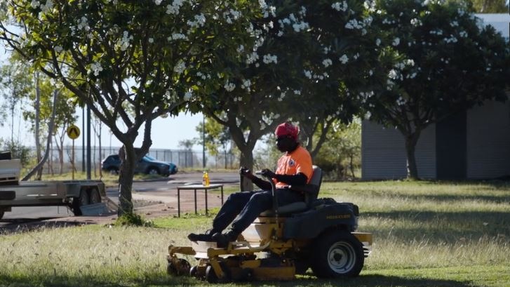 A man rides a lawn mower over grass in Fitzroy Crossing
