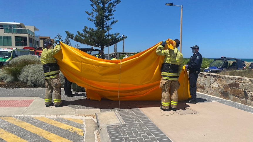 Two men in high vis hold an orange tarp. A police officer stand nearby