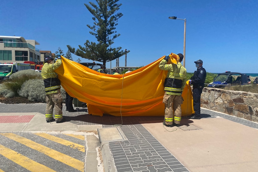 Two men in high vis hold an orange tarp. A police officer stand nearby