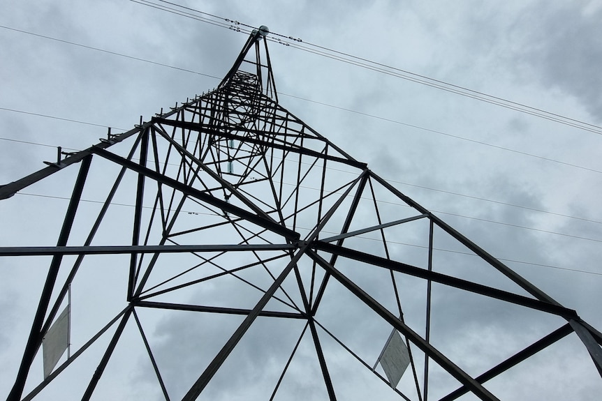 Super low, wide-angle perspective of a tower holding transmission lines with grey, moody sky