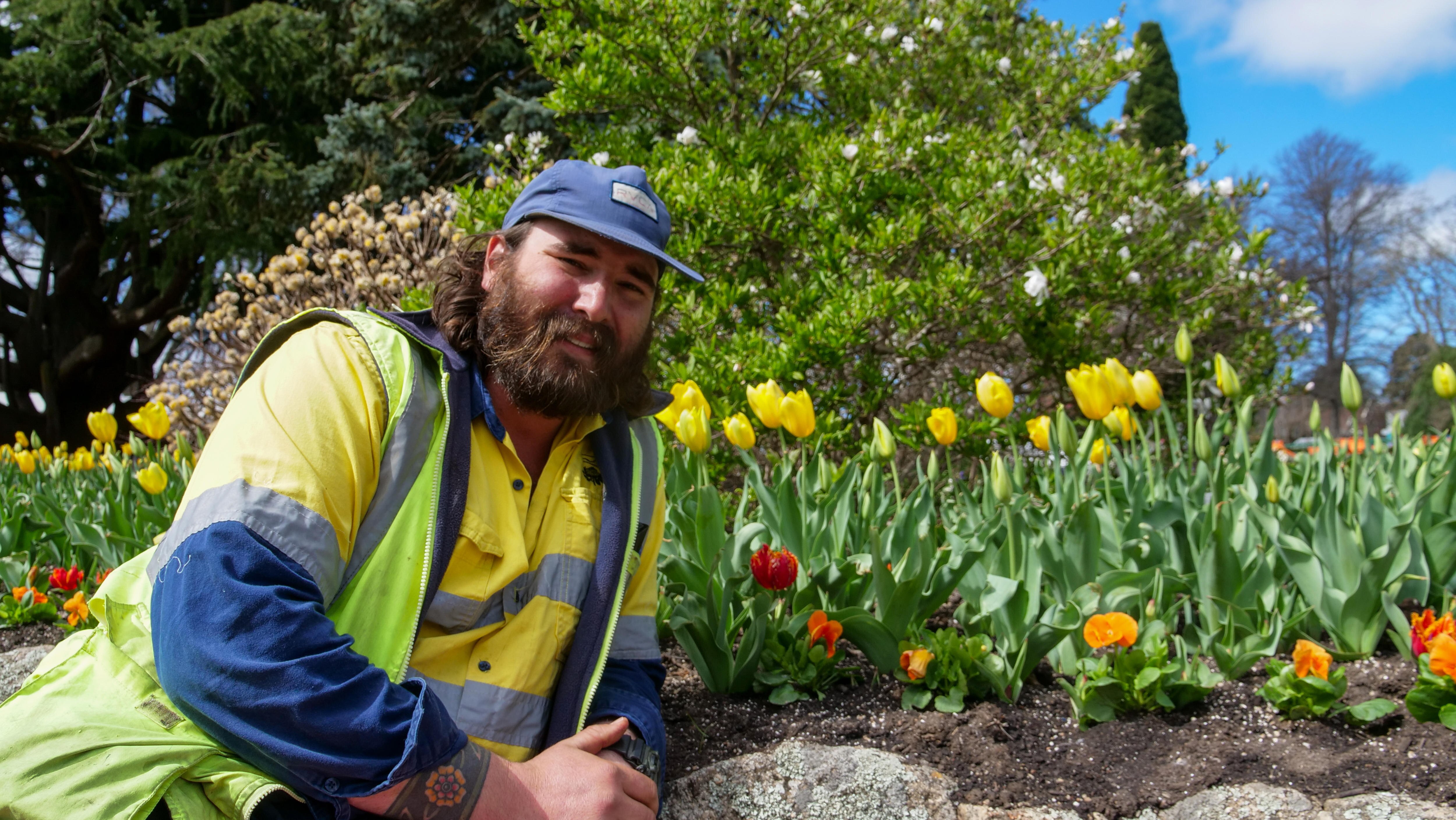 A man wearing gardening gear lounges in front of a garden bed.