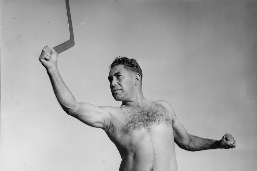 A 1930s black and white photo of an Aboriginal man shirtless and about to throw a boomerang