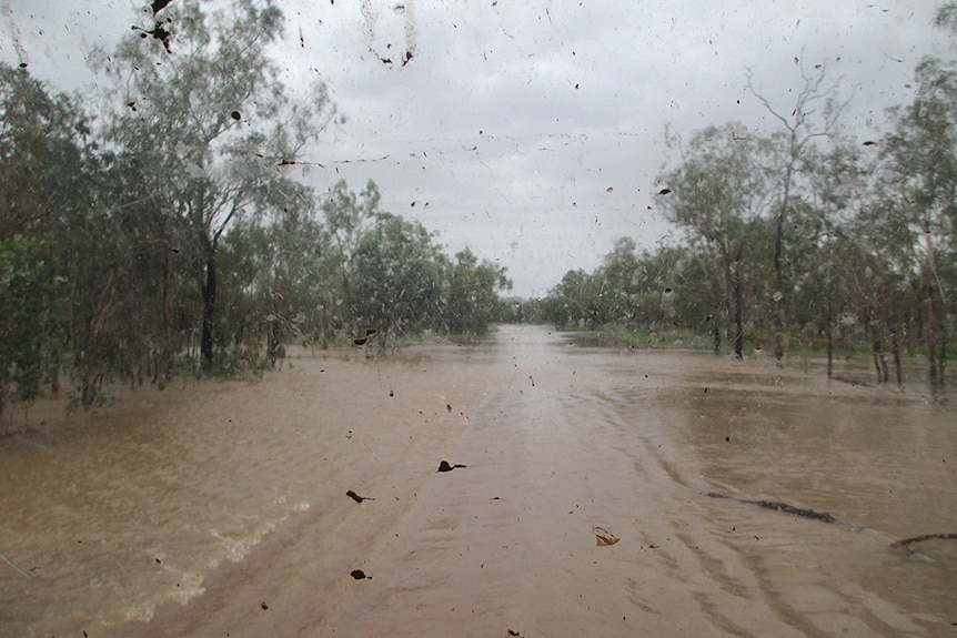 A flooded road taken from the inside of a car, brown floodwaters span either side of the road.