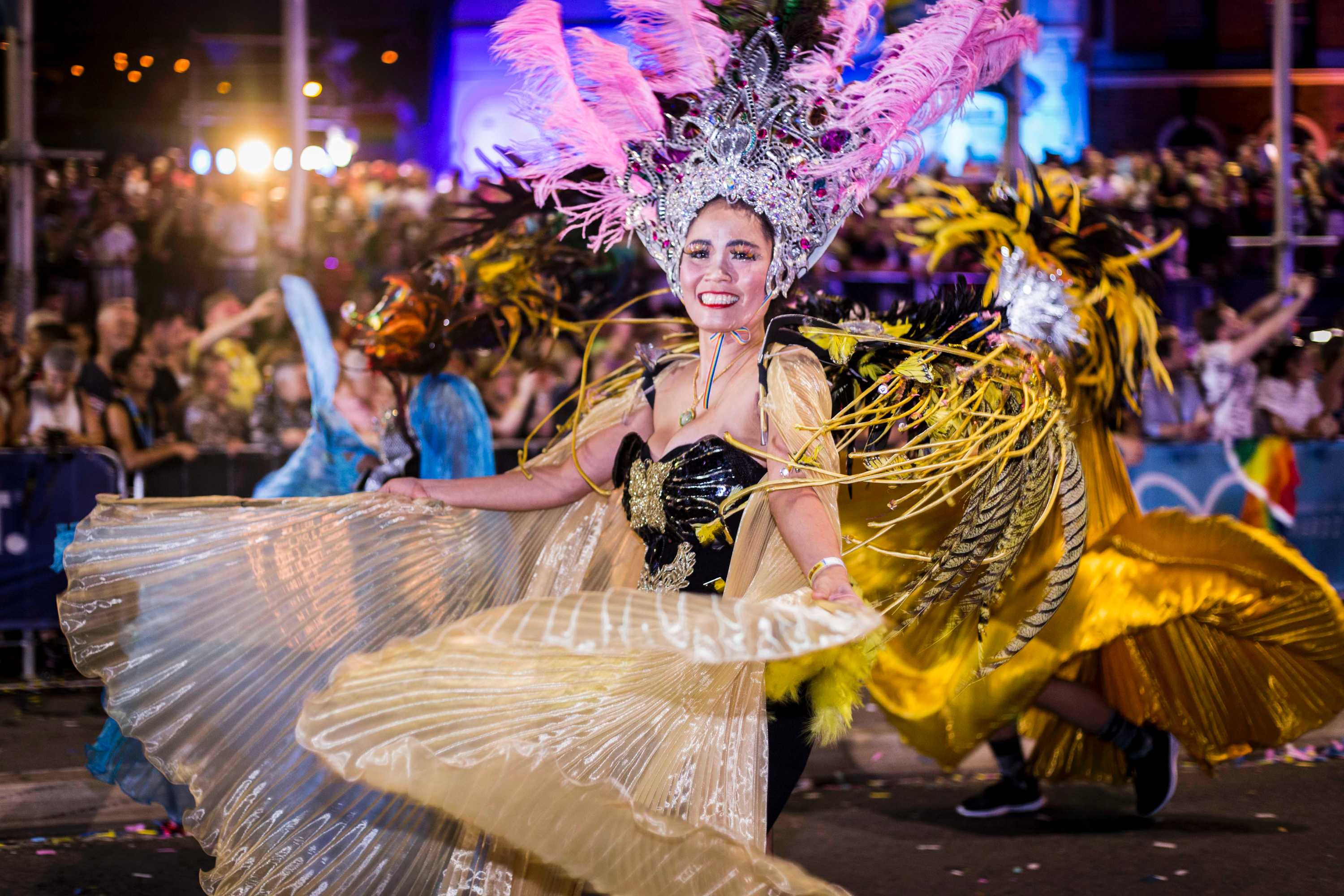 asian woman in feathers twirling a flowing dress in the parade and smiling
