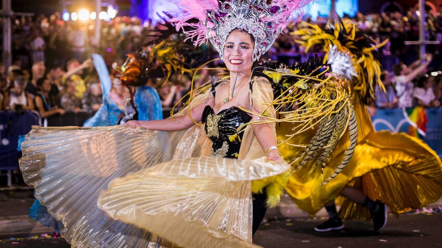 asian woman in feathers twirling a flowing dress in the parade and smiling