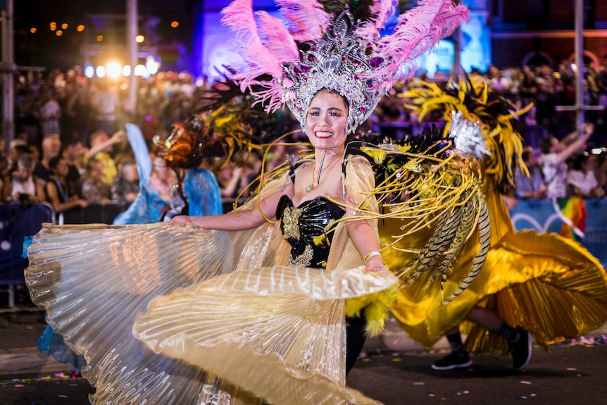 asian woman in feathers twirling a flowing dress in the parade and smiling