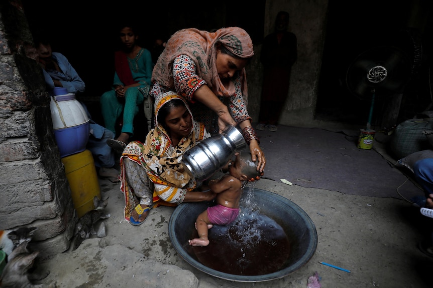 A woman helping the mother of an infant while she bathes her.