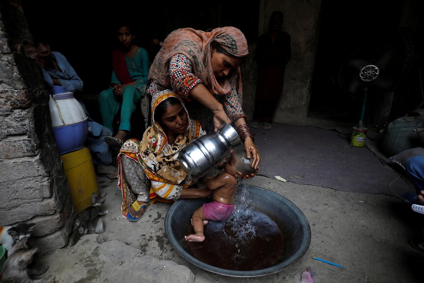 A woman helping a mother of an infant as she bathes her.