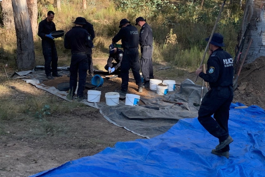 Police officers stand around a ditch looking at the contents of buckets.