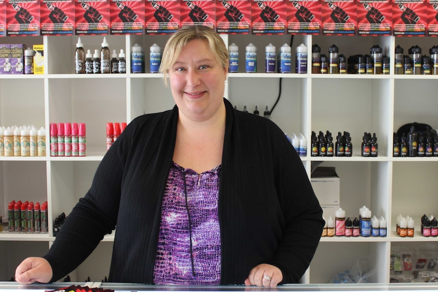 Narissa Hansen standing at the counter of her vape shop, in front of shelves lined with products.