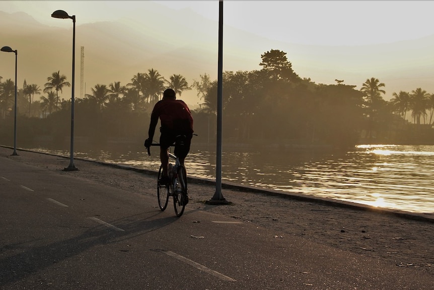 Person cycles away from camera on road near water