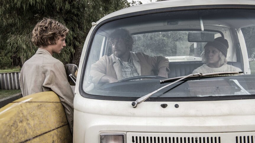 Colour photograph of Simon Baker and Ben Spence sitting in a parked van having a tense chat to Samson Coulter holding his board.