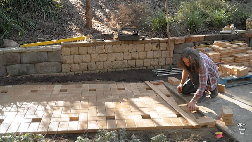 Costa laying pavers in a garden to make a path.