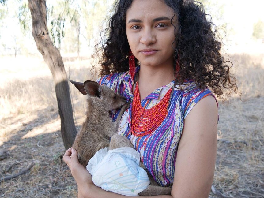 A young woman holds a baby wallaby wearing a disposable nappy.