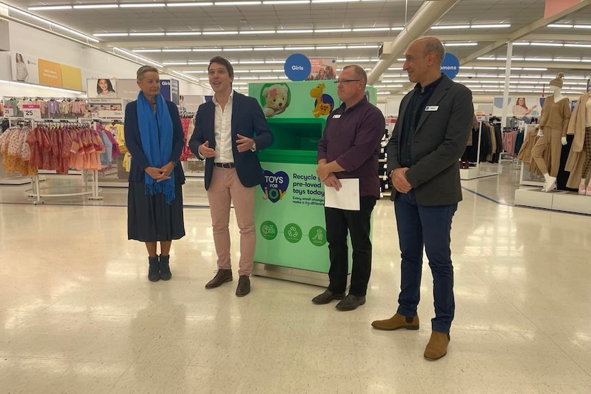 a woman and three men stand in front of green bin in middle of big W store