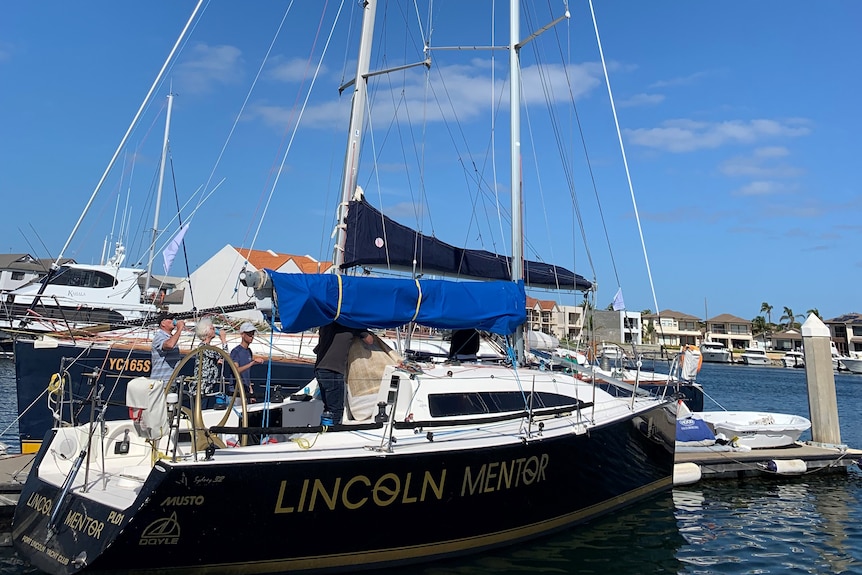 A yacht with Lincoln Mentor written on the helm in harbour with blue water.