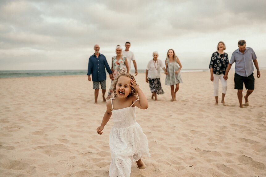 Ruby Pringle runs along the beach with family behind her.