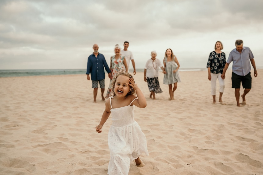 Ruby Pringle runs along the beach with family behind her.