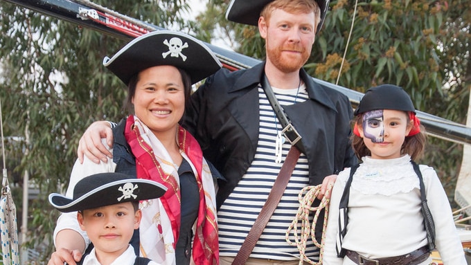 A family stand on a yacht in pirate costume, trees in background.
