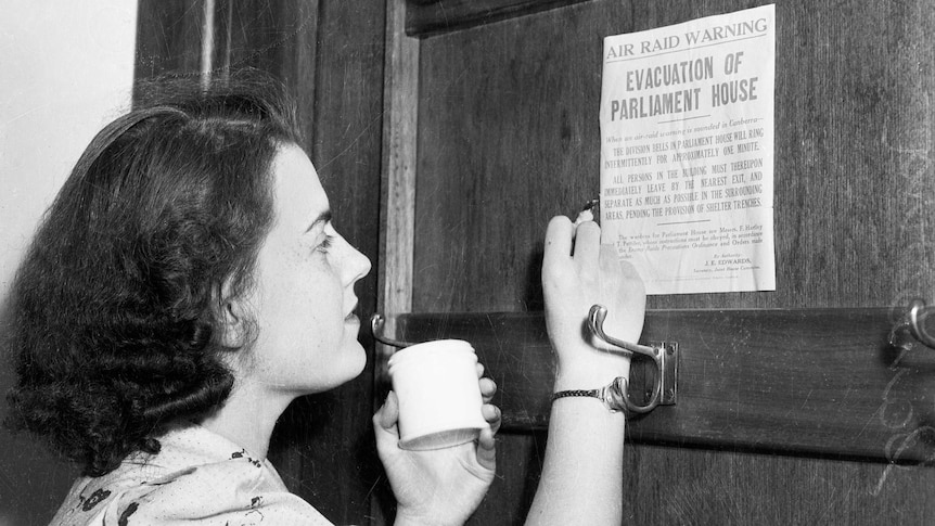 A member of the staff at Parliament House glues an air raid warning sign on a door.