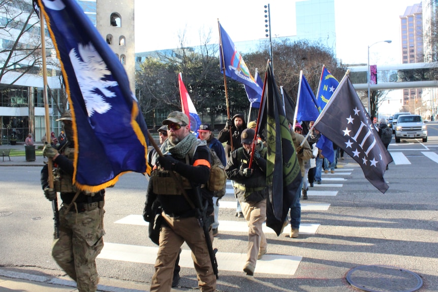 people in camo and carrying guns and flags walk across a street in Richmond