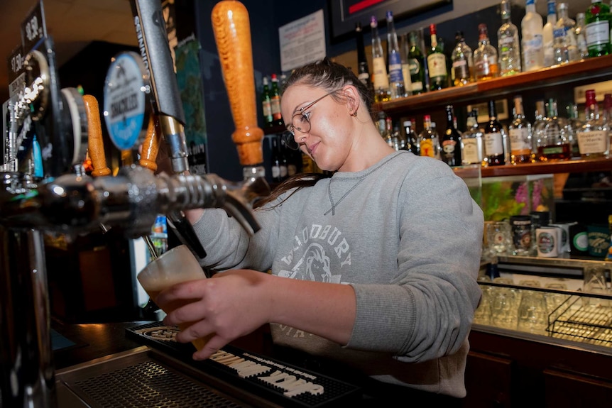 A woman pours a pint of beer behind a bar.