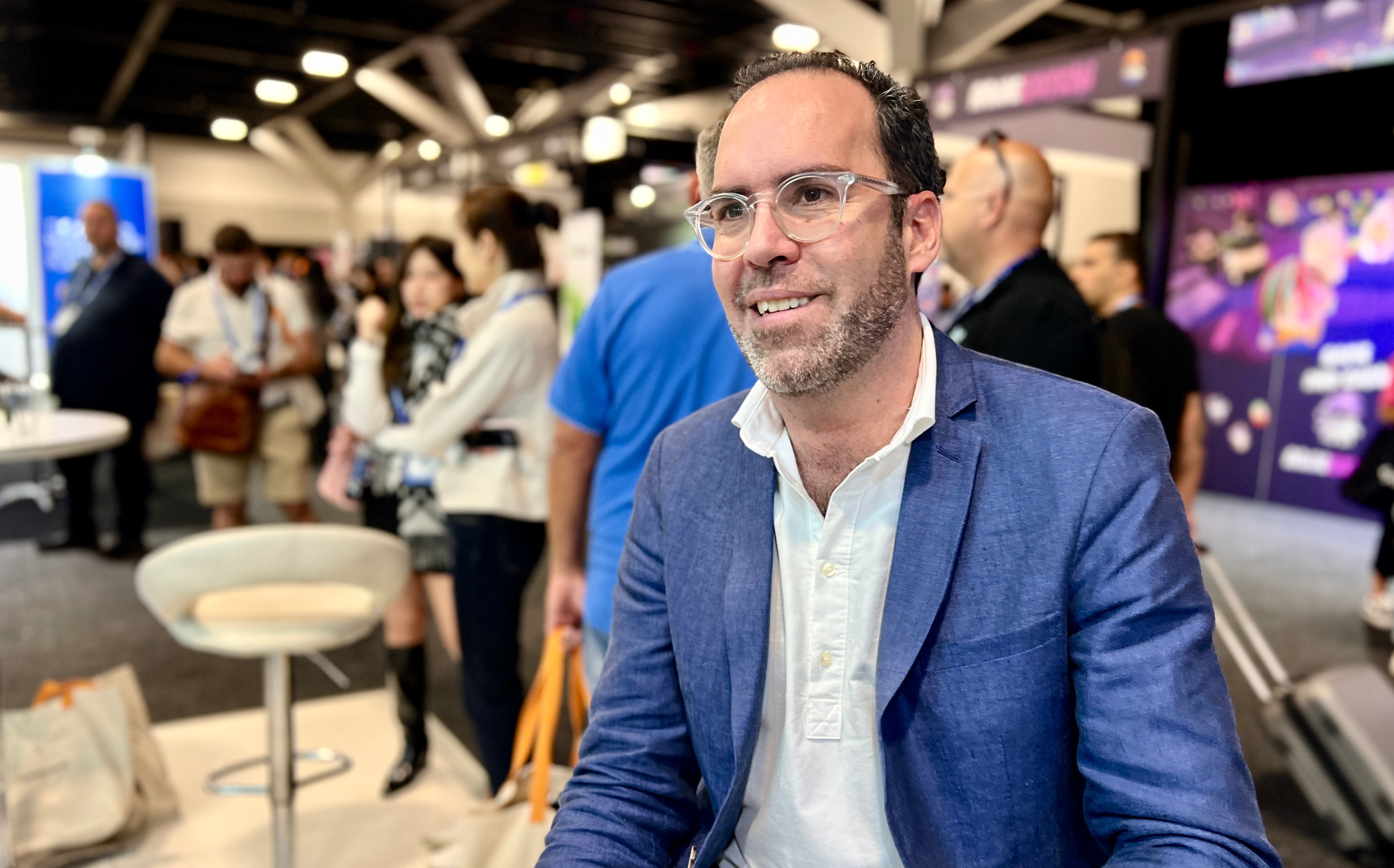 Man in blazer with glasses smiles past the camera.