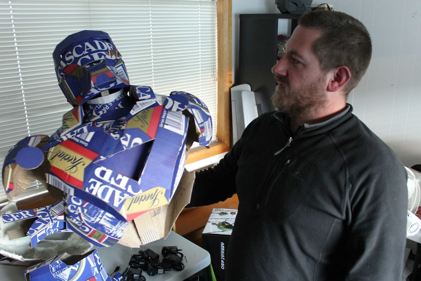 Rian Taylor holding a replica ironman suit made from beer cartons, 12 August 2014.