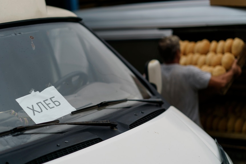 A car windshield with russian writing on it, a man carrying bread in the background