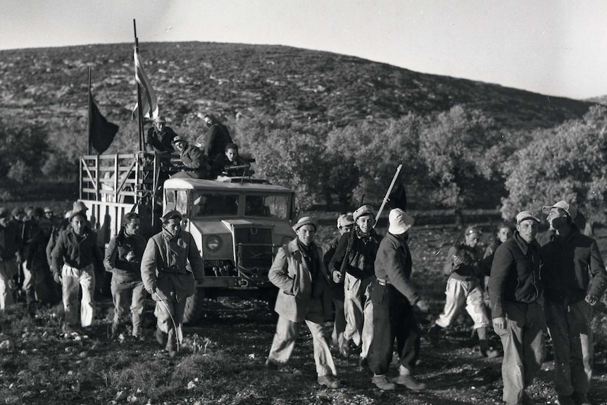 Workers walk along a path with a truck carrying supplies, on the way to Kibbutz Yasur.