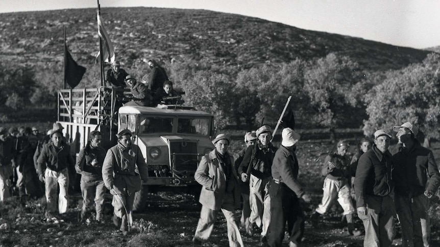 Workers walk along a path with a truck carrying supplies, on the way to Kibbutz Yasur.